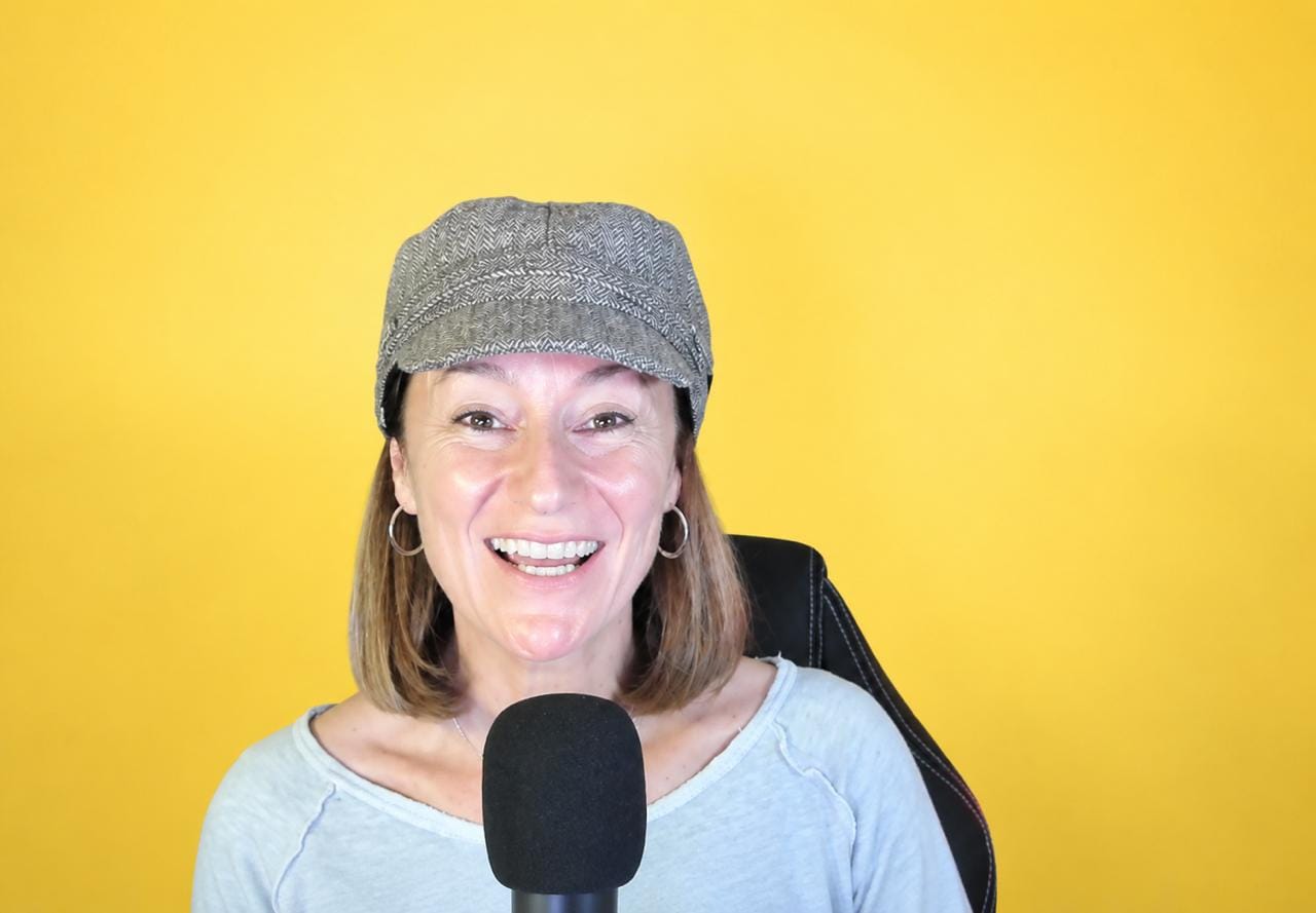 Alegría ante un micrófono, con gorra gris y fondo amarillo.